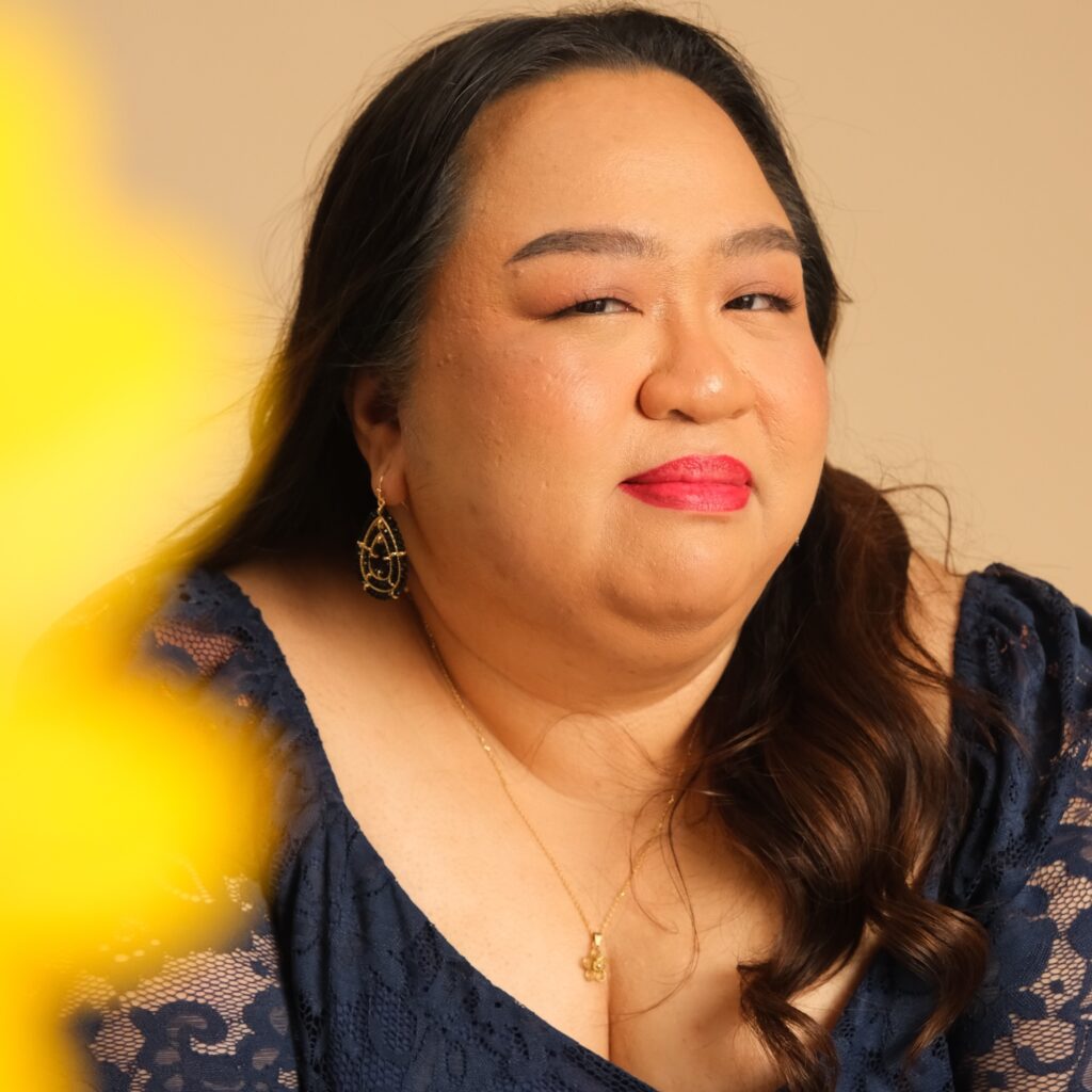 he poet, a Filipino woman with long dark hair, looks at the camera with a slight smile. She is wearing a black dress and a small pendant on a gold chain.