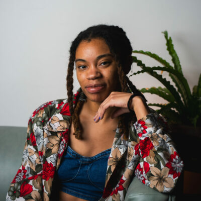 A headshot of the author Jae Nichelle, a Black woman with locs, sitting down and smiling at the camera.