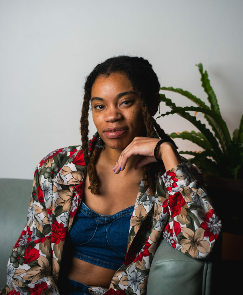 A headshot of the author Jae Nichelle, a Black woman with locs, sitting down and smiling at the camera.