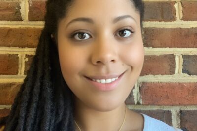 An African-American woman smiles while standing in front of a brick wall.