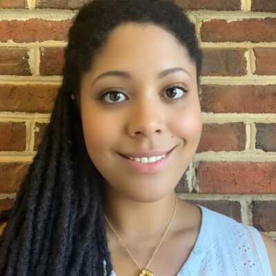 An African-American woman smiles while standing in front of a brick wall.