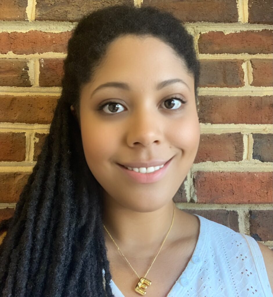 An African-American woman smiles while standing in front of a brick wall.