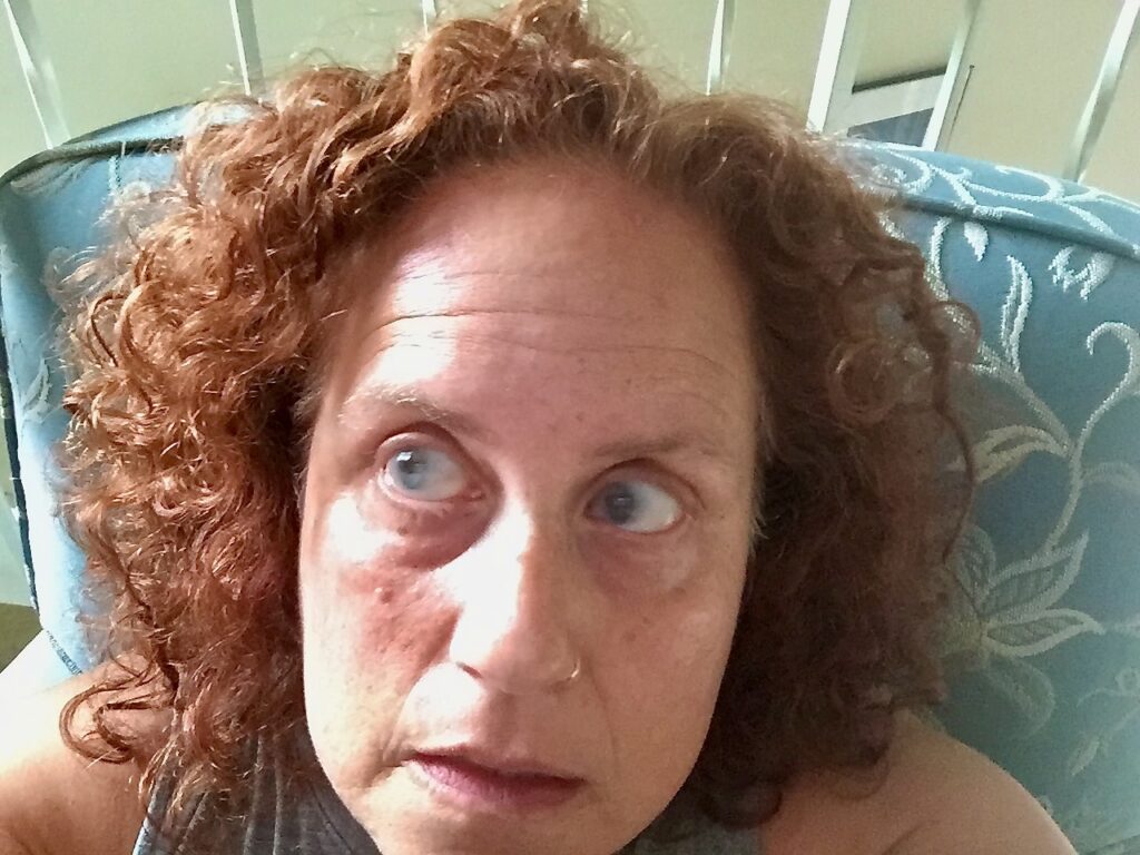 Close-up of Becka Mara McKay, a Caucasian woman with curly reddish-brown hair, looking off to the side. There is a turquoise blue couch cushion behind her.