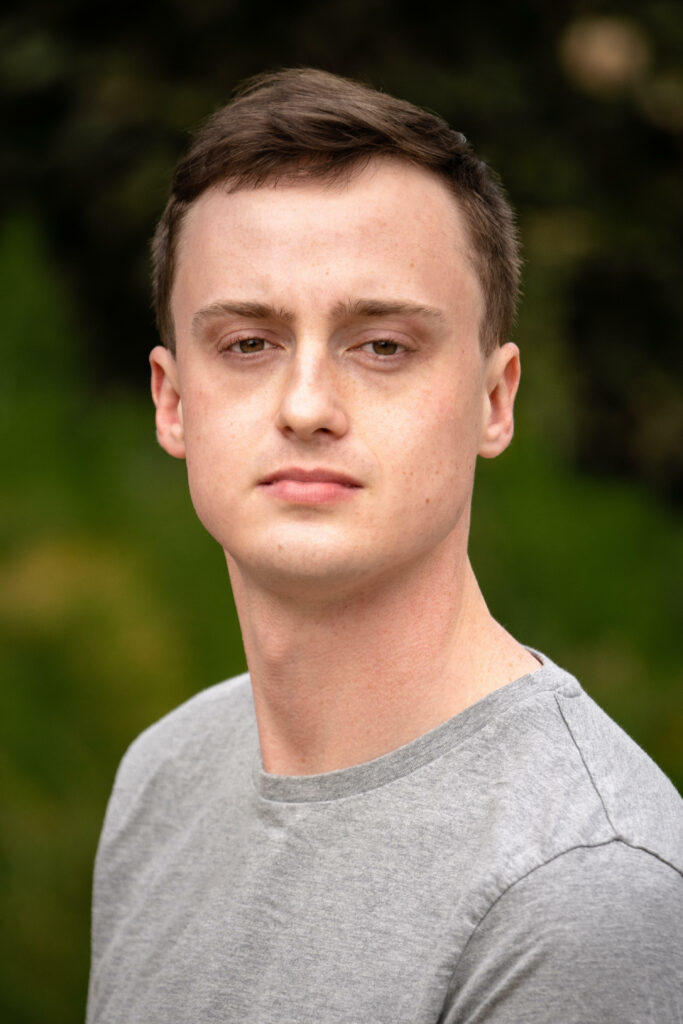 William Ward Butler, a Caucasian male, stands outdoors, face turned to look at the camera. He wears a grey tshirt.