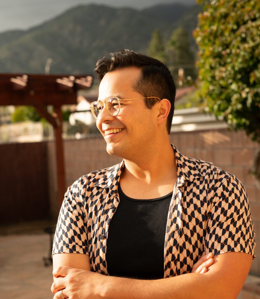Nathan Xavier Osorio wears an unbuttoned short-sleeved print shirt and a black tee shirt. He has short black hair, wears glasses, and is smiling off-camera to the side.