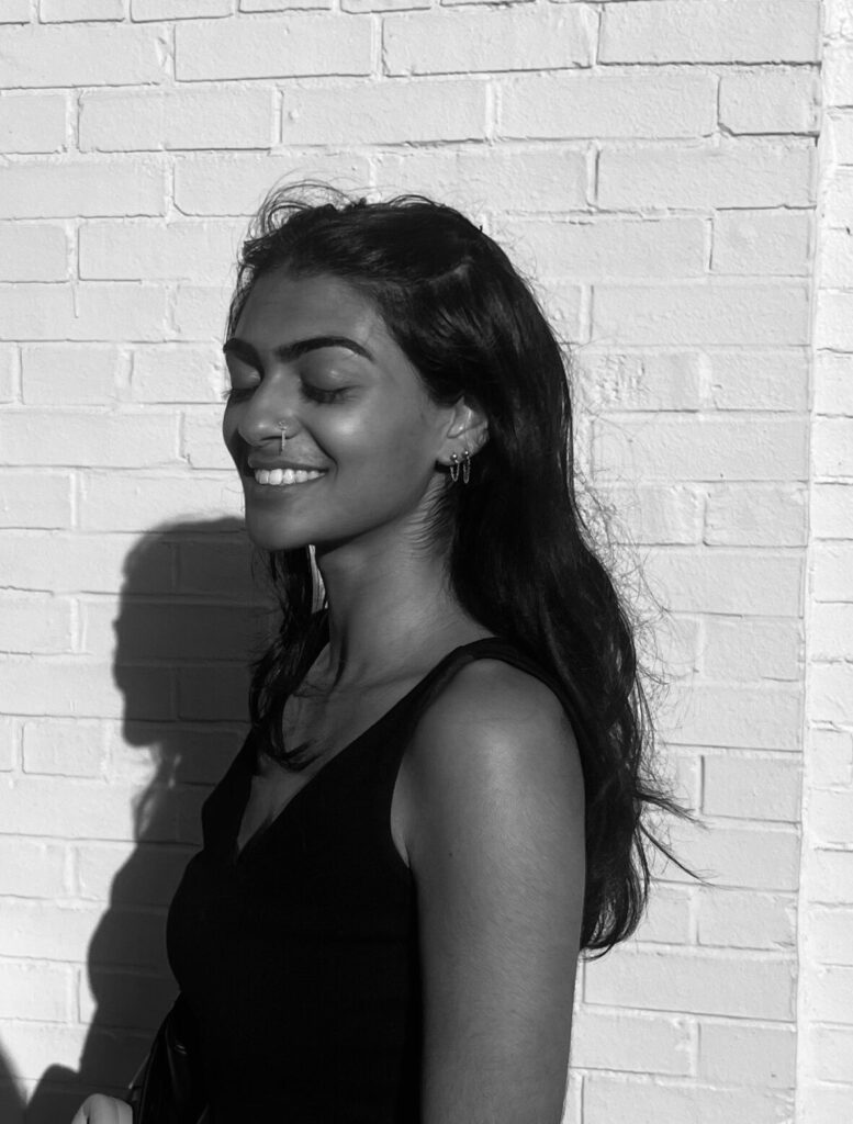  A side profile of a poet smiling with her eyes closed. Her shadow is behind her against a brick wall. 