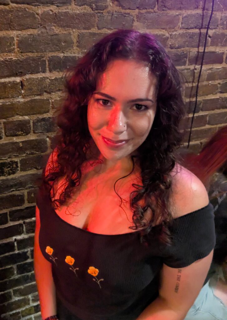 A white woman with curly brown hair and wearing a black shirt smiling up at the camera.